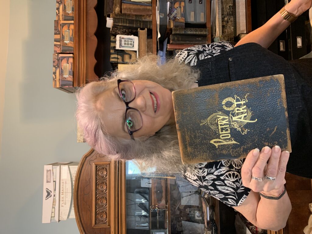 A picture of me, Robyn Hood Black, in my studio holding the cover of an antique book with gilded letters reading "Poetry & Art."